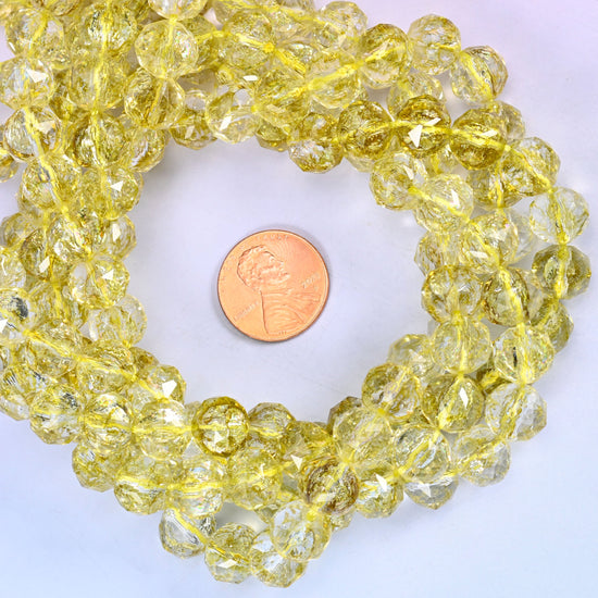 Transparent lemon yellow faceted round glass bead strands coiled around a US penny for size reference