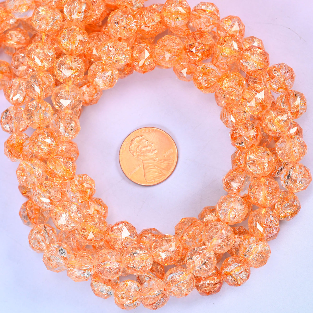 Transparent orange faceted round glass bead strands coiled around a US penny for size reference