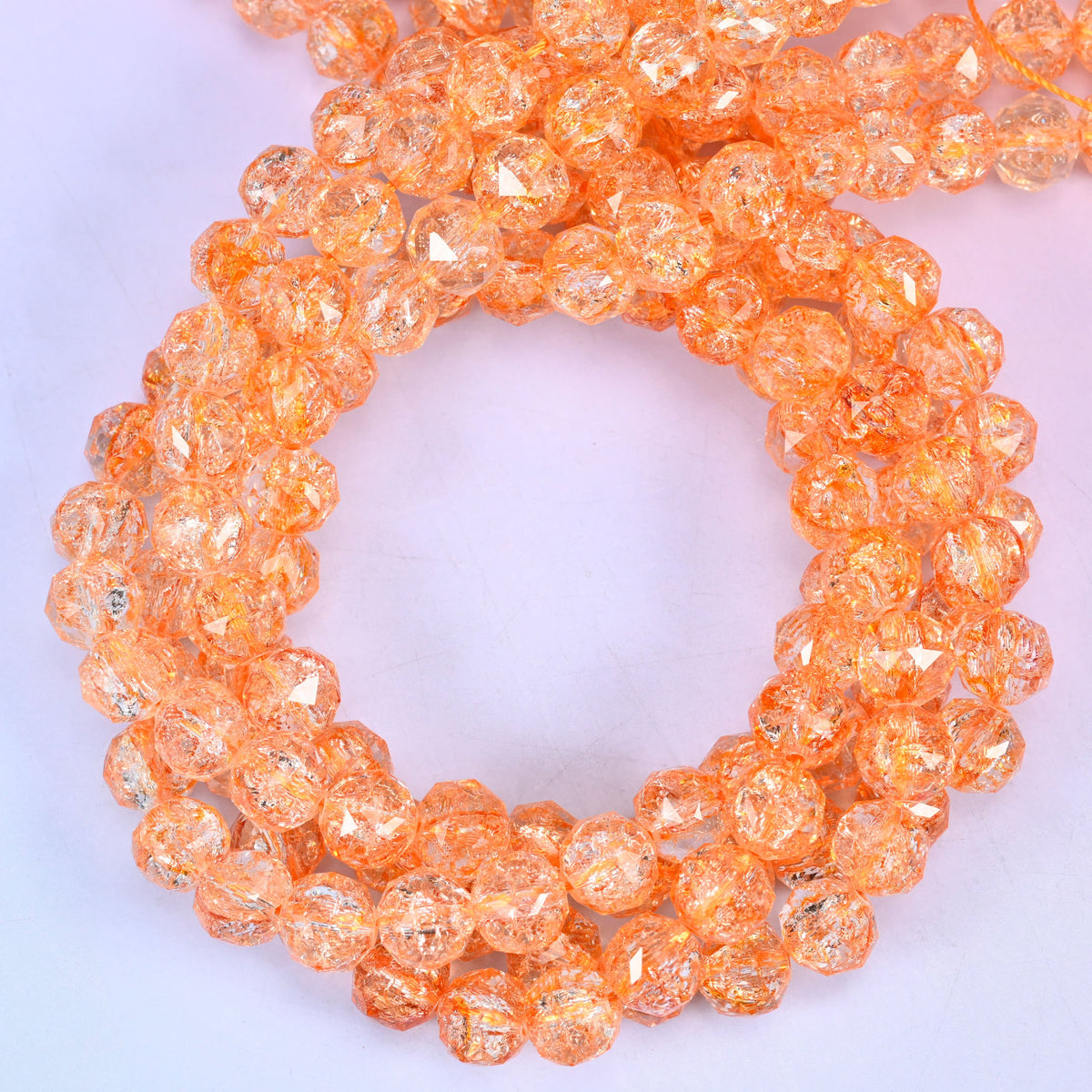 Transparent orange faceted round glass beads, close view of the coiled strands showing clear peachy orange