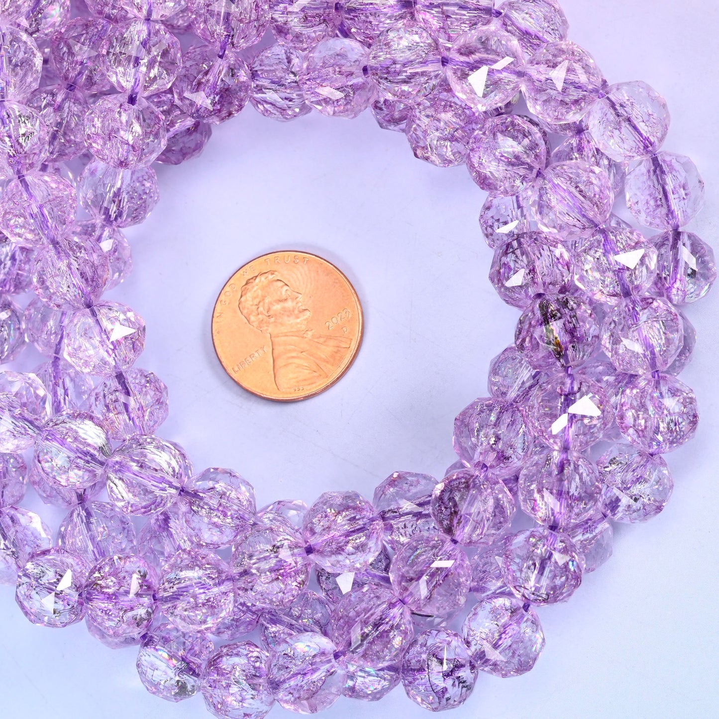 Transparent purple faceted round glass bead strands coiled around a US penny for size reference