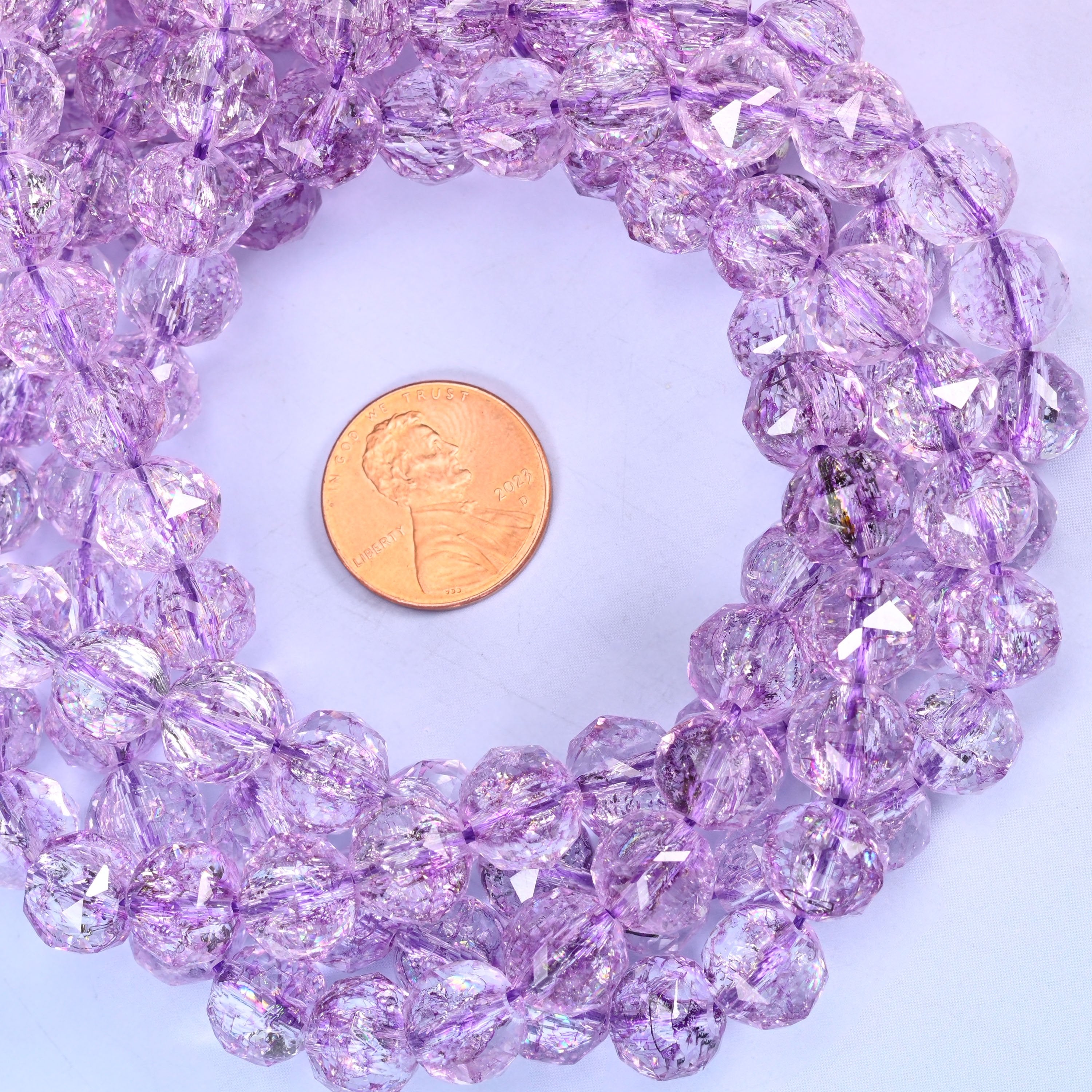 Transparent purple faceted round glass bead strands coiled around a US penny for size reference