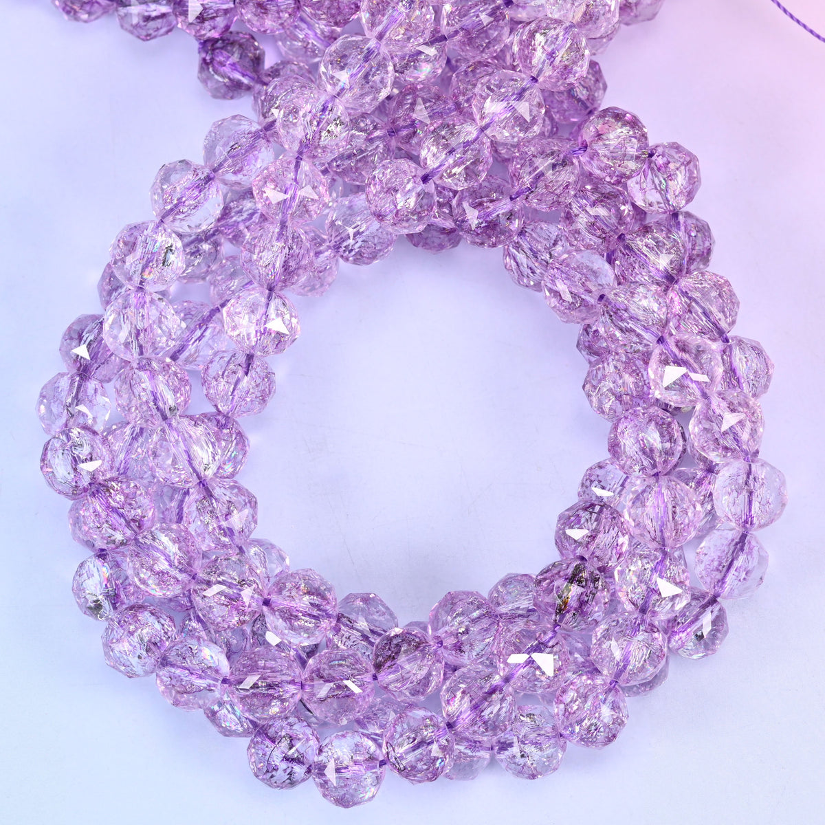 Transparent purple faceted round glass beads, close view of the coiled strands showing clear lilac purple