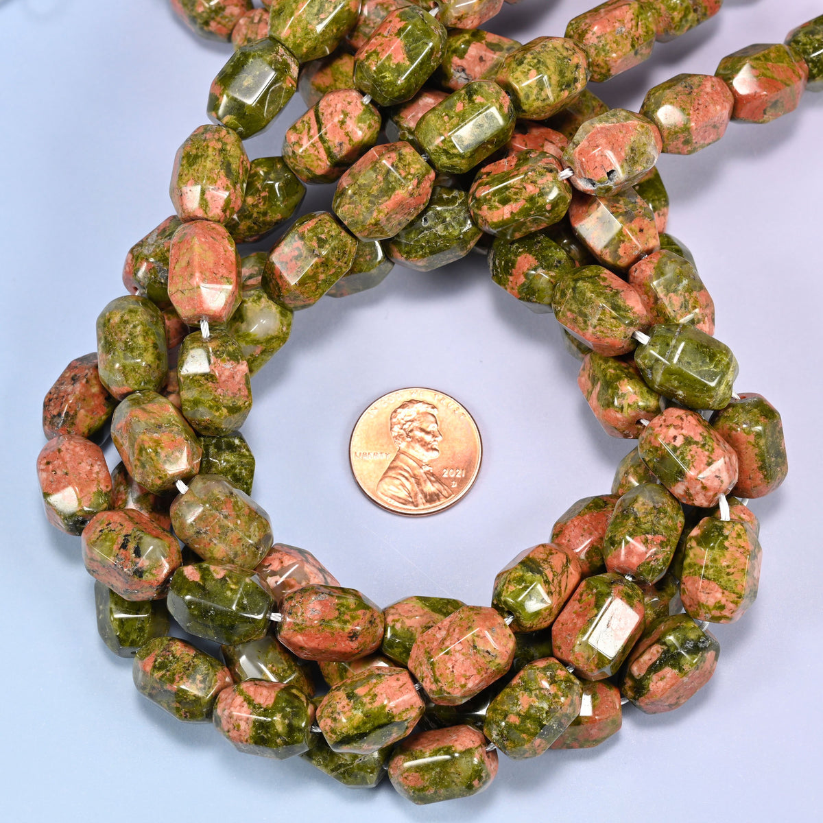 Unakite faceted barrel bead strands coiled around a US penny for size reference