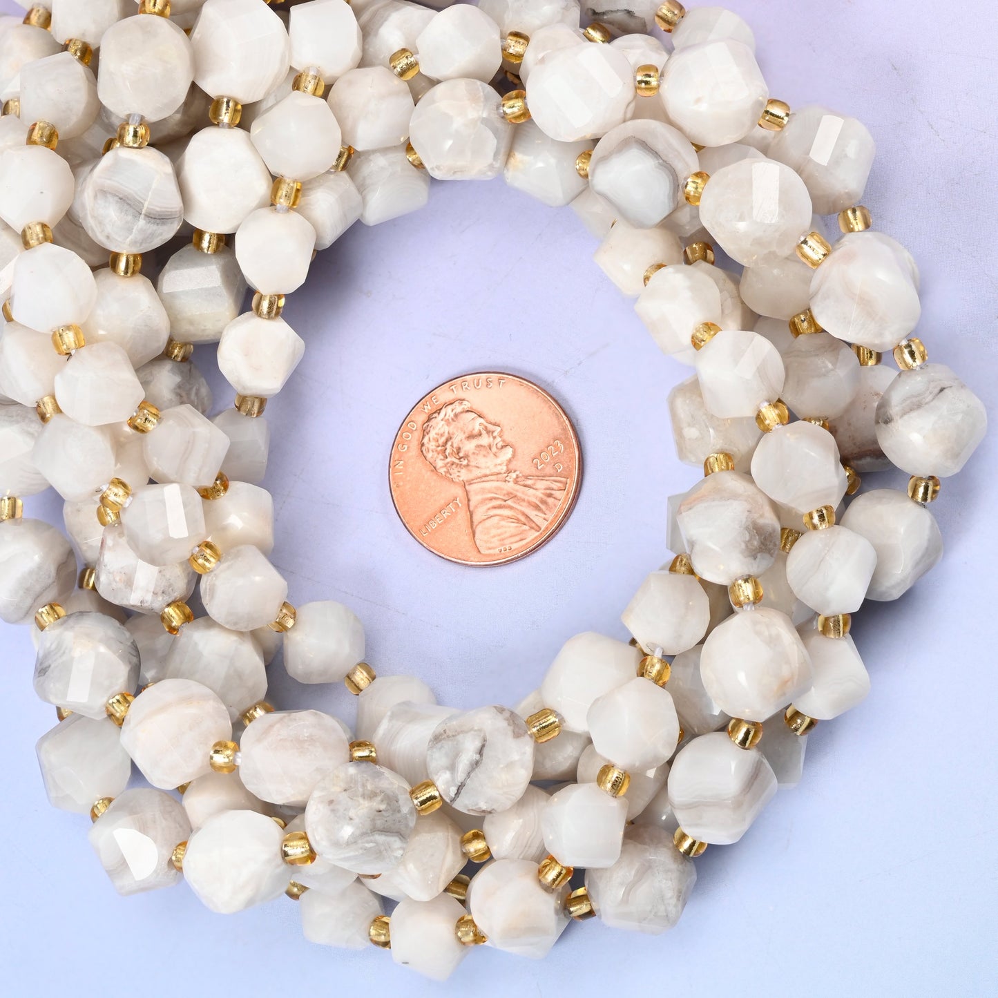 White Crazy Agate faceted spiral twist bead strands coiled around a US penny for size reference