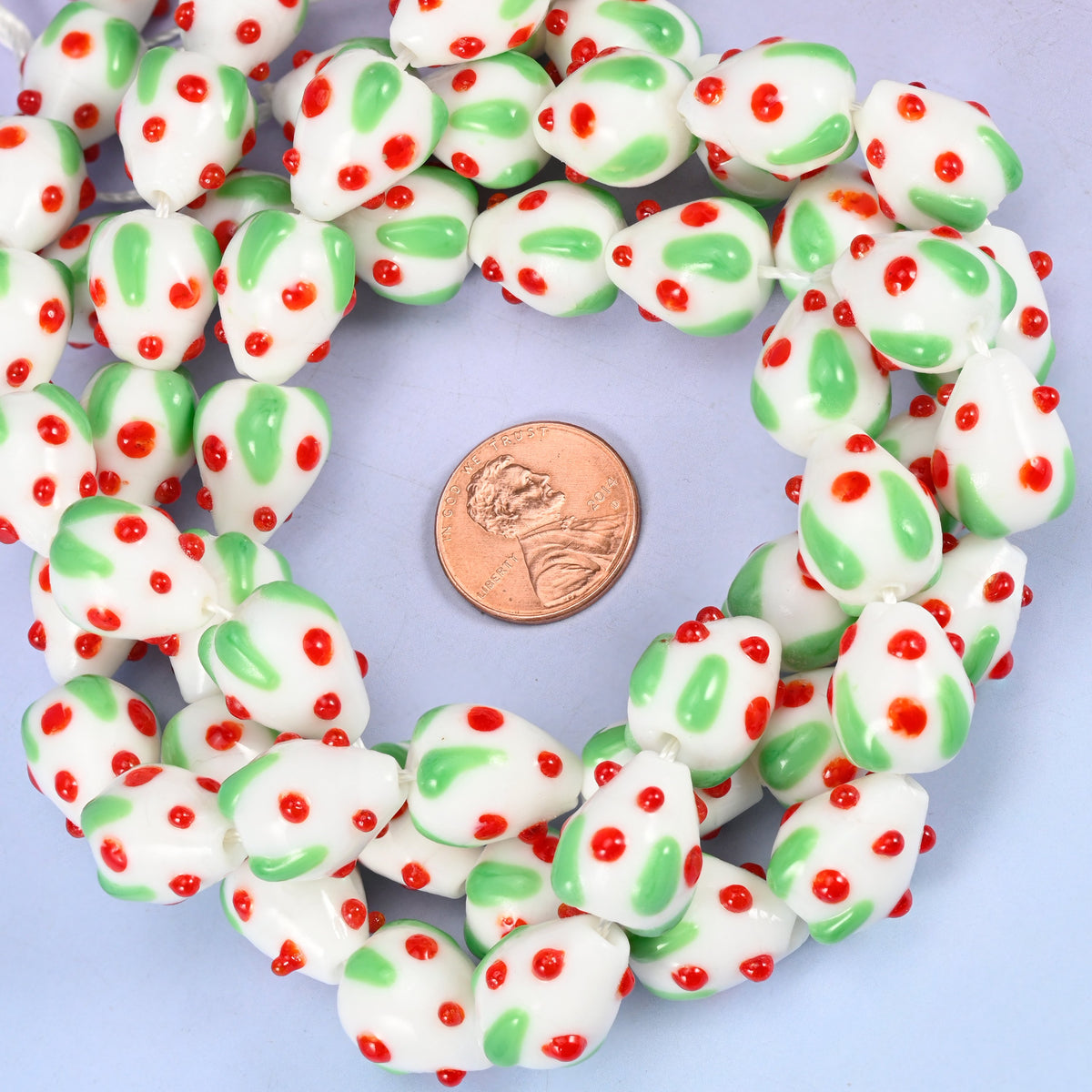 White Red Dots Strawberry glass bead strands coiled around a US penny for size reference