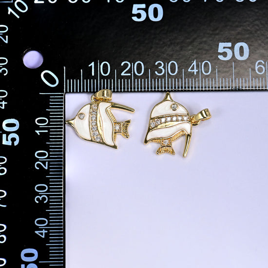 Two tropical fish charms in white enamel with gold fins and clear pave stones, shown front and angled, beside a millimetre ruler for scale