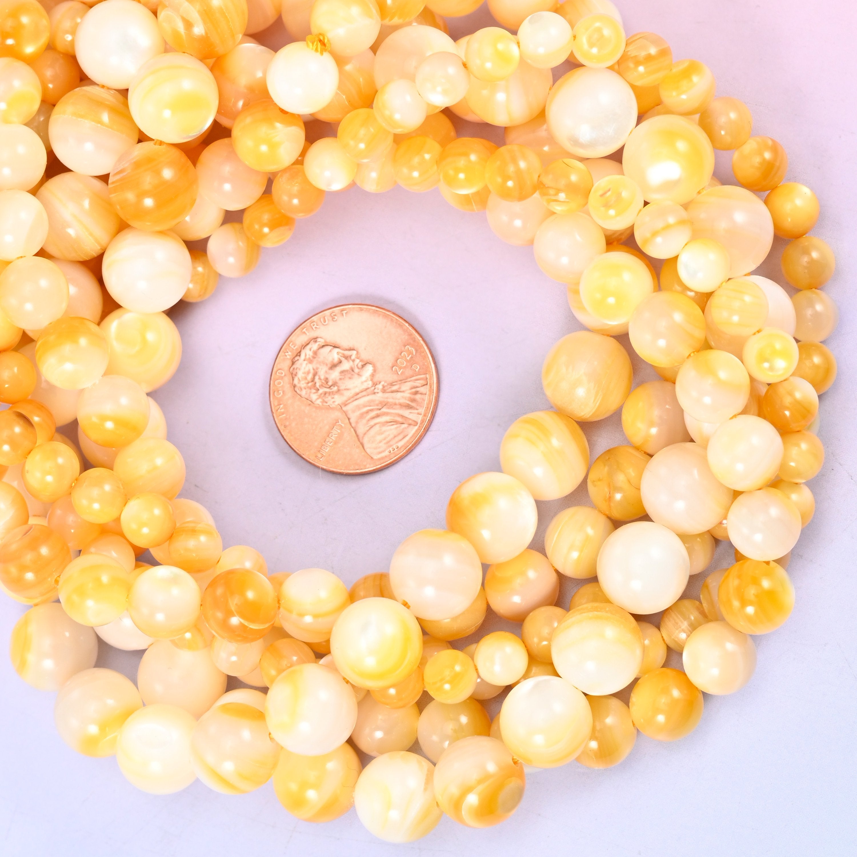 Yellow pearl shell round bead strands coiled around a US penny for size reference