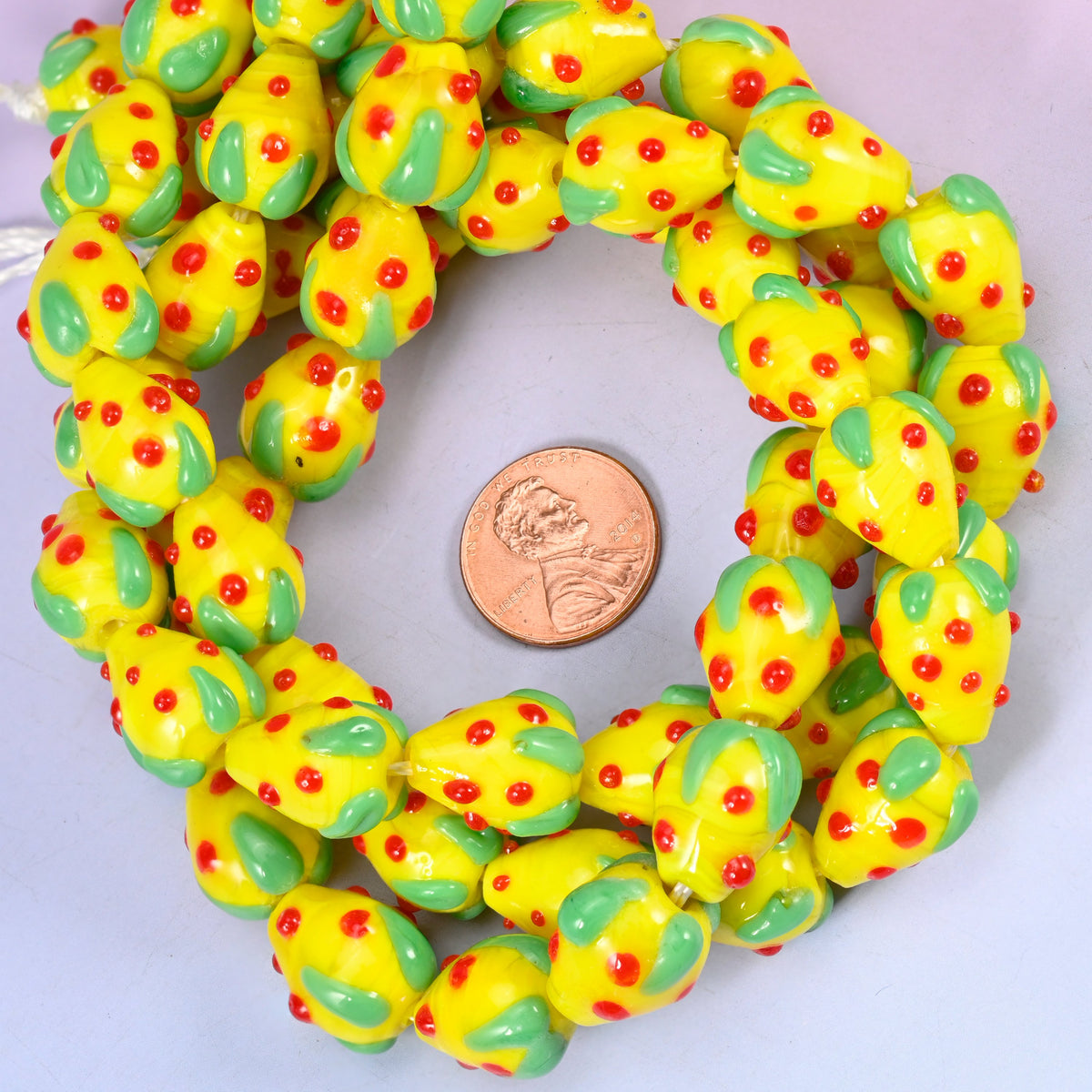 Yellow Red Dots Strawberry glass bead strands coiled around a US penny for size reference
