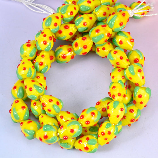 Yellow Red Dots Strawberry glass beads, close view of the coiled strands in yellow with green leaf panels and red seed dots