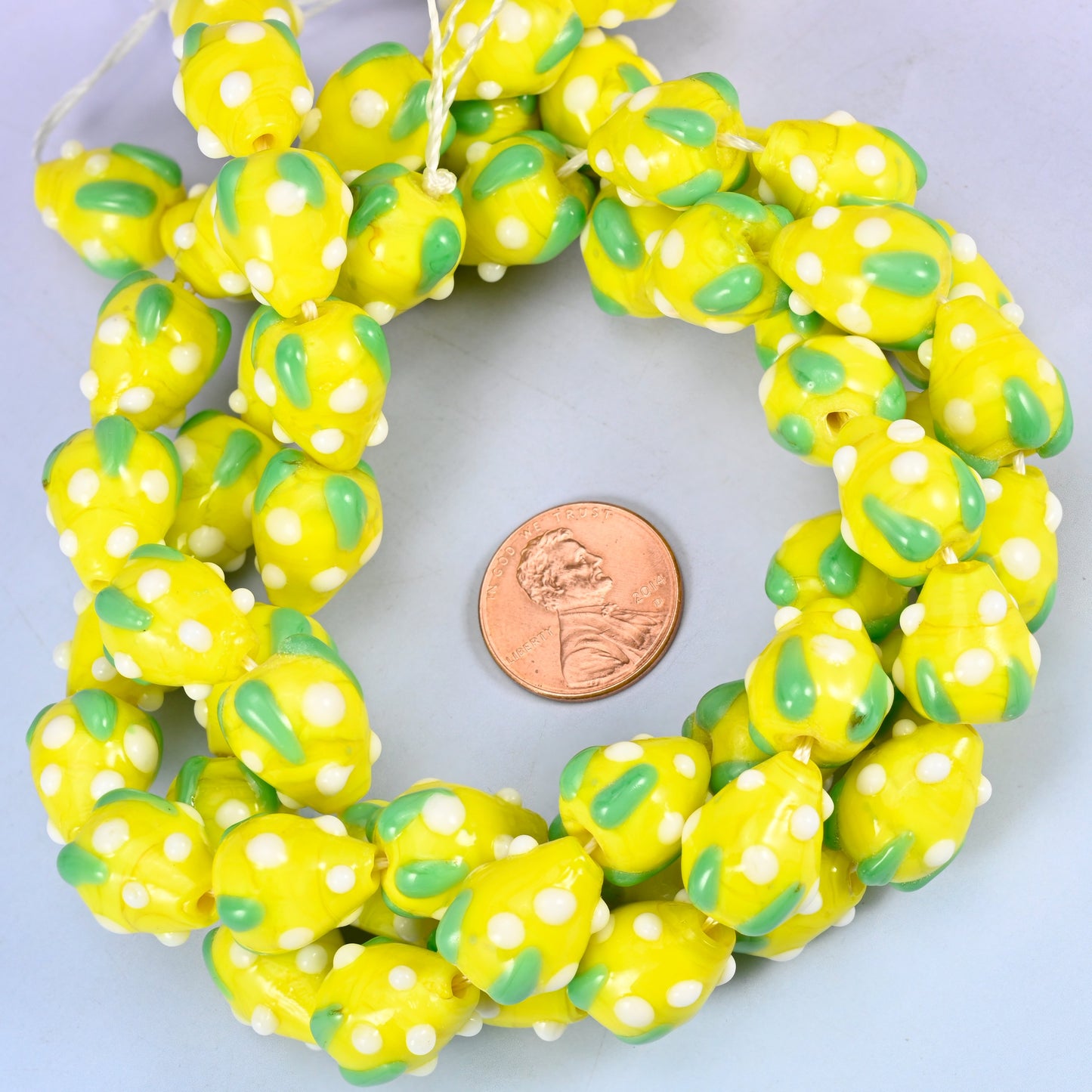 Yellow White Dots Strawberry glass bead strands coiled around a US penny for size reference
