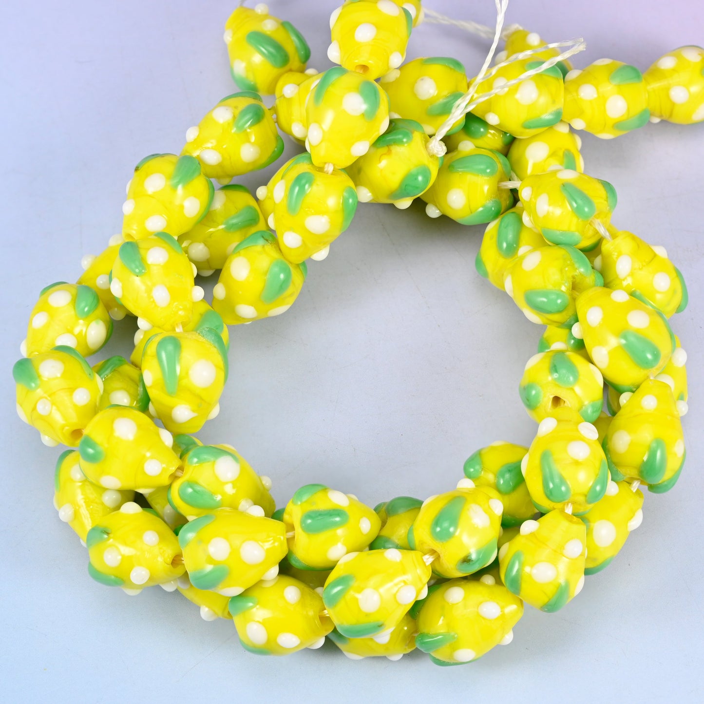 Yellow White Dots Strawberry glass beads, close view of the coiled strands in yellow with green leaf panels and white seed dots